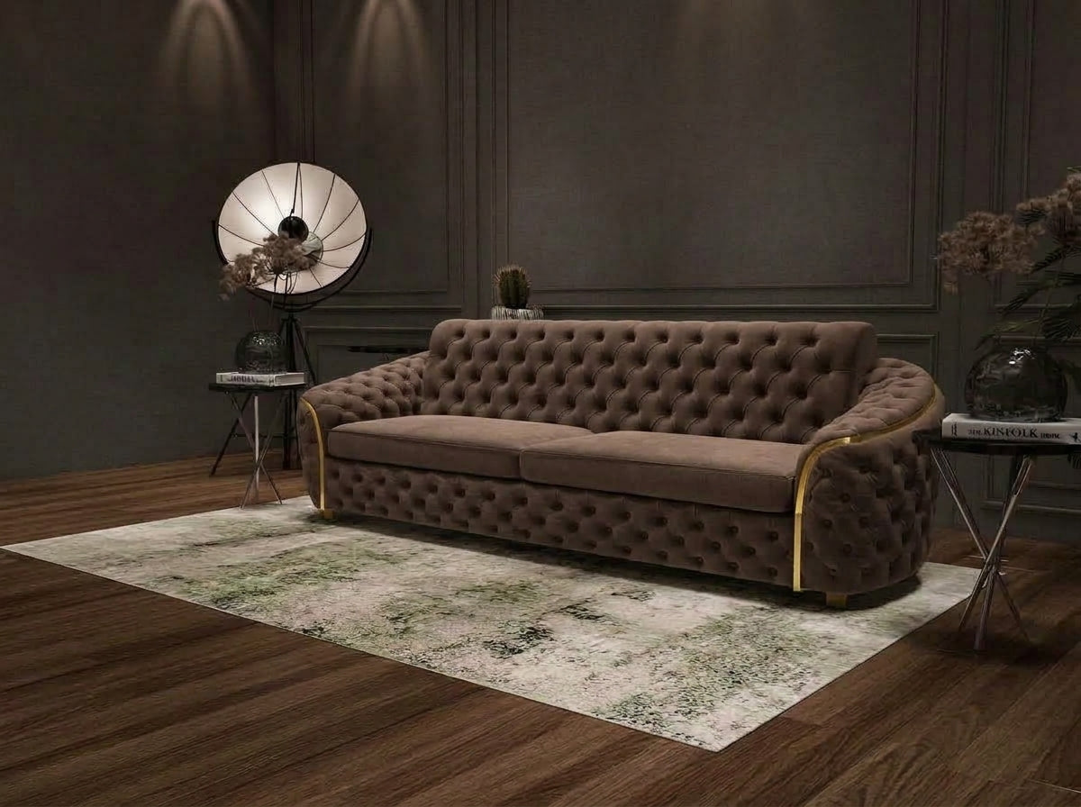 A tufted brown velvet sofa with gold-toned metal arm accents, styled in a modern living room setting on a patterned rug with dark wood flooring.