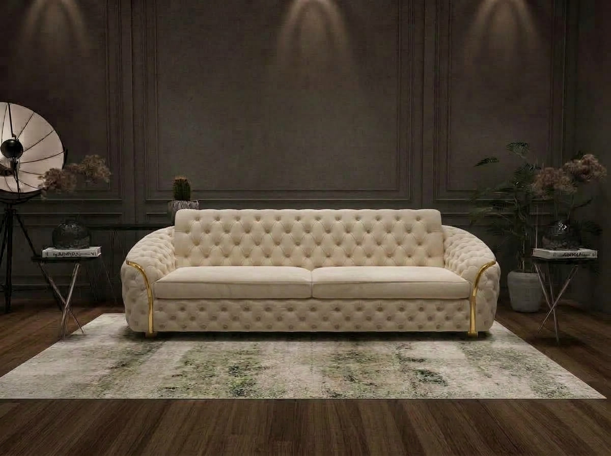 A cream tufted sofa with gold arm accents, placed on a patterned area rug in a dark, elegant room with wood paneling and floor.