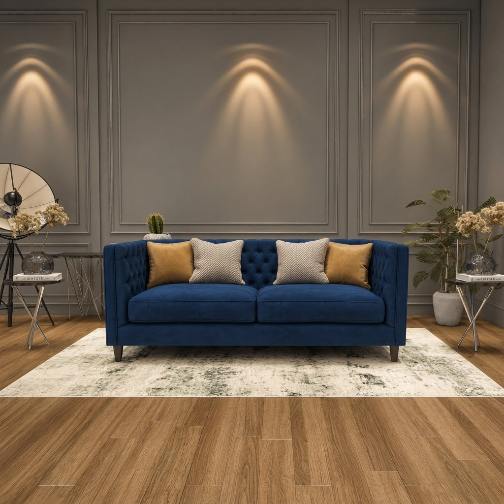 A blue tufted loveseat sofa with four decorative throw pillows, styled on a white and gray patterned area rug in a modern living room setting with wood floors and wall sconces.