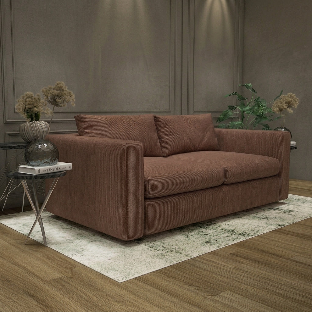 A modern two-seater sofa upholstered in a textured brown fabric, styled in a contemporary living room setting on a light patterned rug with a small side table in the foreground.